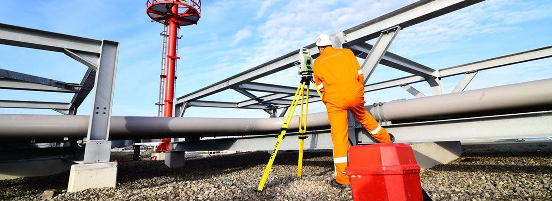 Landmeter voert industriële maatvoering uit met een total station bij een staalconstructie en leidingwerk.